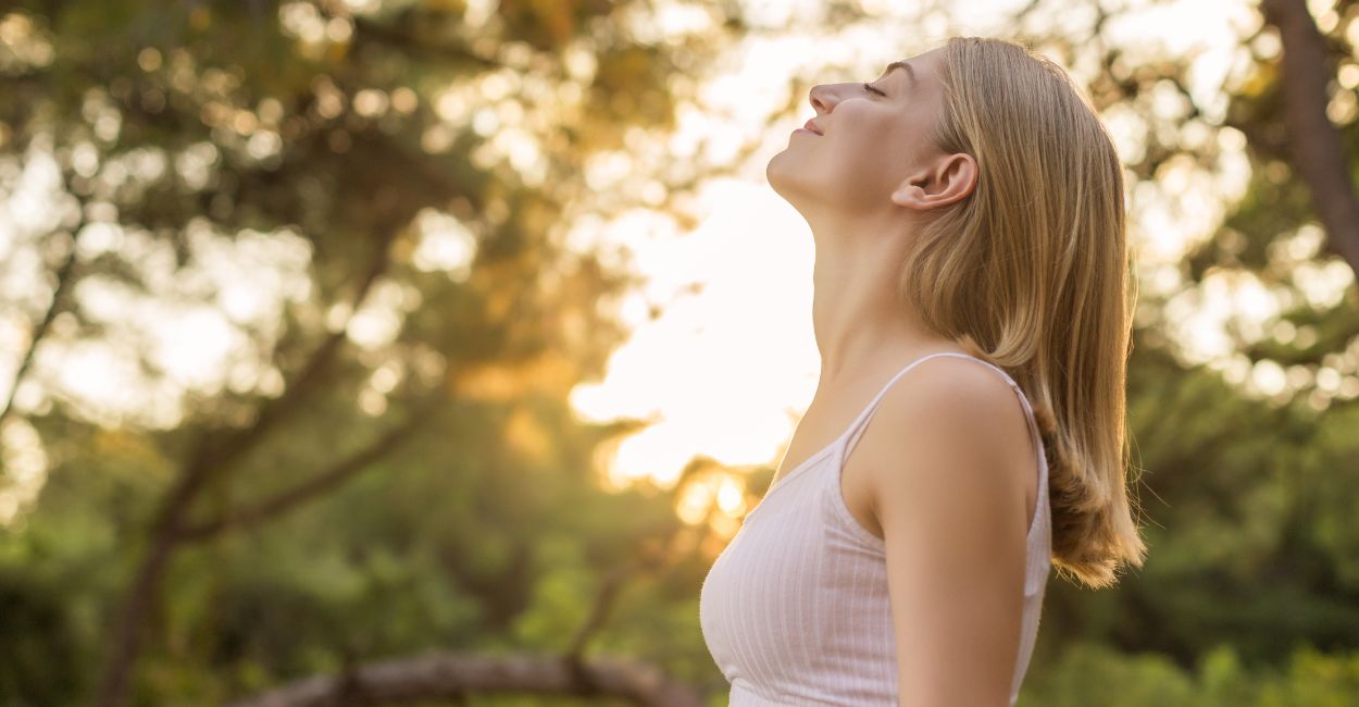 Mulher em meio à natureza respirando fundo em um momento de paz interior 
