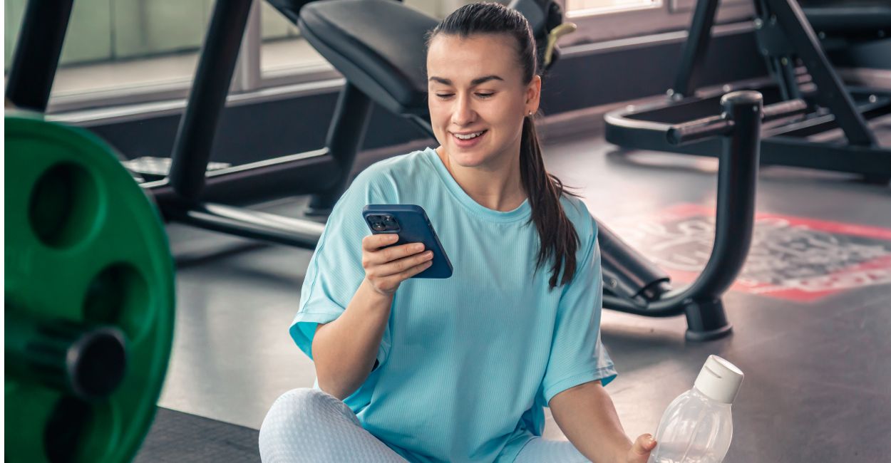 Mulher jovem na academia calculando imc pelo celular